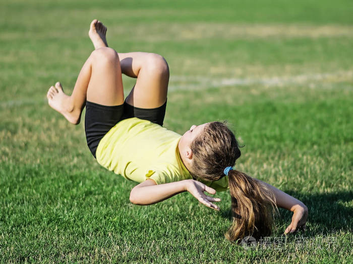 运动的小女孩后翻跟头落在草上.失去平衡在空气中