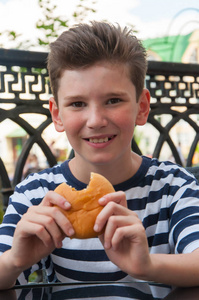 一个时髦的发型和汉堡包的年轻微笑的男孩