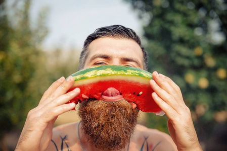 一个人与一个时尚的发型 长长的胡须和纹身非常高兴地吃西瓜