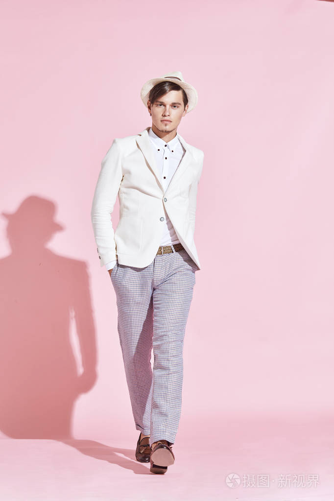 年轻英俊严重现代男模特穿着白色夹克, 白衬衫, 灰色裤子和步进在工作