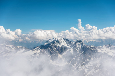 深蓝色的天空，云在山的多岩石的山峰上覆盖着冰川和积雪