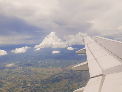 飞翔的云与土地飞机机翼。人们看着天空从飞机的窗口