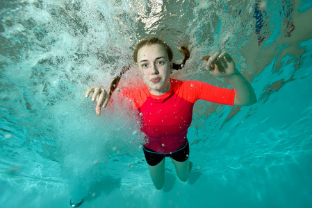 漂亮的女孩在红色泳衣水下游泳在蓝色的背景上,看着我照片
