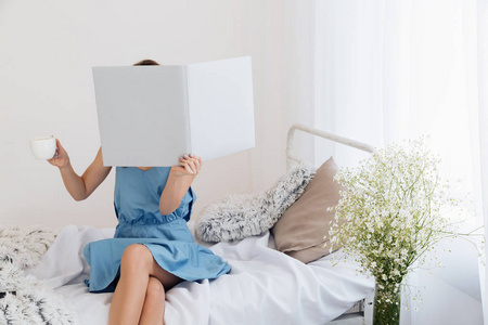 坐在床上喝咖啡的书遮住脸的女人