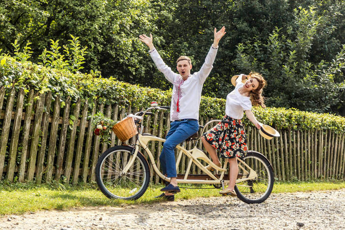 对年轻情侣在公园自行车串联.在他们的手和微笑,年轻人保持帽子.