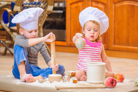 两个兄弟姐妹男孩和女孩在厨师的帽子坐在厨具