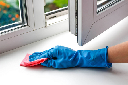 女性在蓝色的橡胶手套的手擦玻璃。洗白塑