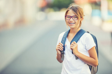 现代快乐的青少年学校女孩的包,背包里的肖像.牙齿矫正眼镜的女孩照片