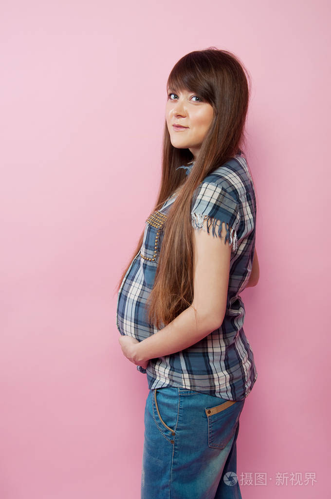 怀孕的妇女,穿着牛仔裤和格子的衬衫,抱着她的肚子