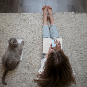 可爱的金发美女在智能手机上使用社交媒体。坐在家里的地板与那只猫。从山顶