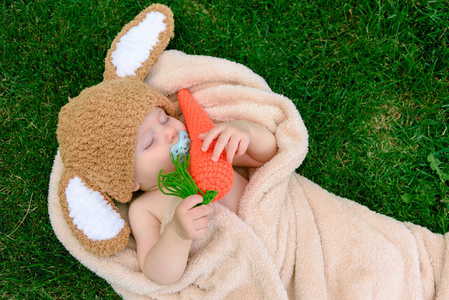 像一只小兔子与胡萝卜玩具上绿草户外帽子的婴儿