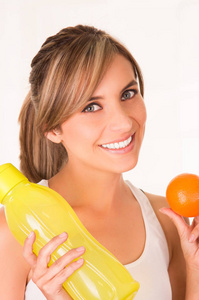 年轻美丽的女人微笑着身穿白色 t 恤和保持健康的橙色和黄色瓶水的特写