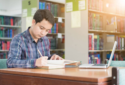 年轻的学生在图书馆从一本书笔记