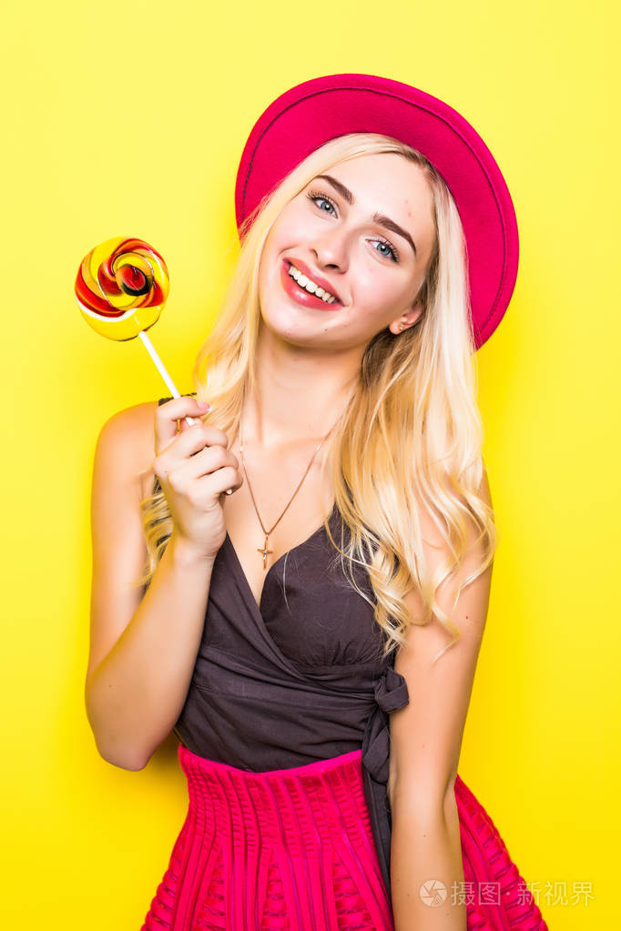 棒棒糖在黄色背景上的漂亮金发性感美女