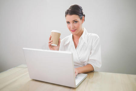 漂亮的女商人用笔记本电脑拿咖啡