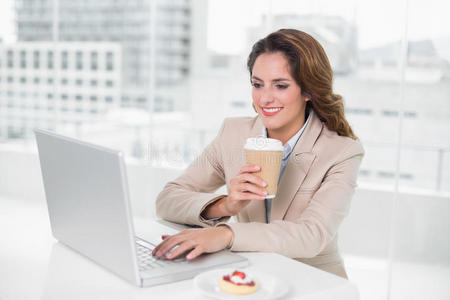 女商人在办公桌旁用笔记本电脑喝咖啡