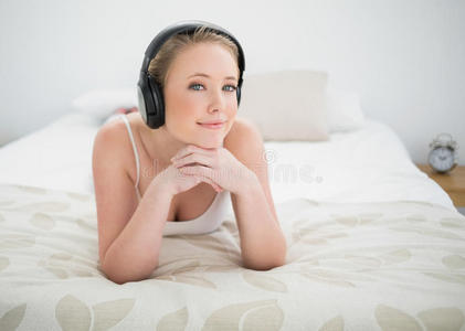 自然微笑的金发女郎躺在床上听音乐