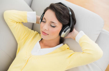 黄色开襟羊毛衫的休闲黑发女郎，戴着耳机听音乐