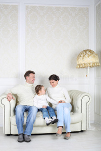 一家人穿着白色毛衣和牛仔裤坐在白色沙发上