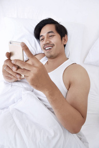亚洲男子躺在床上与智能手机
