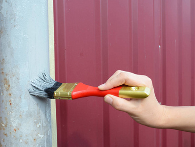 画篱笆的油漆工人手的金属栅栏.用红色画笔绘画篱笆照片