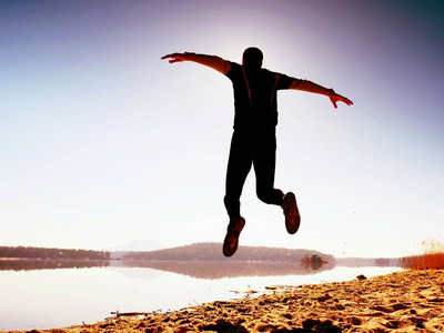 运动员在地平线日出期间在海滩上飞照片