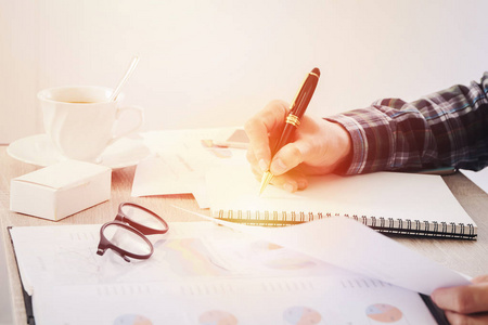 手中商人写东西笔记本纸,和桌上模糊的业务财务报告文件照片