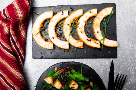 温暖南瓜沙拉配芝麻菜，叶混合甜菜，在灰色的背景上的黑色板板上。烤的南瓜。顶视图