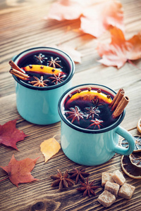 在蓝色漆包乡村杯子与香料和柑橘类的水果上的木桌和秋天的落叶的甜酒。复古色调