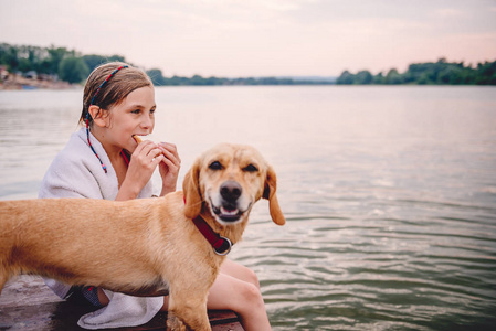 女孩坐在船坞与她的狗和吃三明治在河