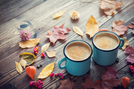 在蓝色的搪瓷的杯和秋天的落叶木桌上的咖啡