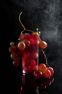 一杯葡萄浆果 红酒与一串葡萄在黑色的背景与鼓的滴