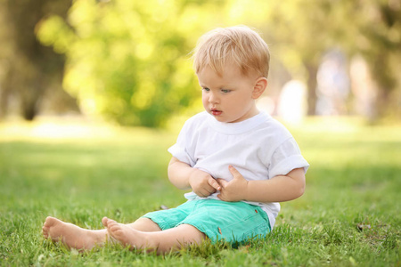 可爱的小宝贝男孩坐在公园里的绿草上