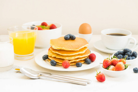 与蓝莓草莓和黑咖啡牛奶和橙汁在白色石头桌背景的健康早餐设置与薄饼和麦片