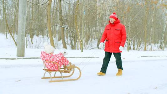 愉快的小男孩在雪撬在冬天公园与他的祖父