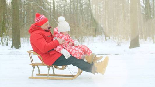 快乐的小男孩和他的祖父在冬天公园的雪橇上