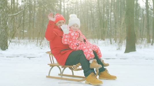 快乐的小男孩和他的祖父在冬天公园的雪橇上