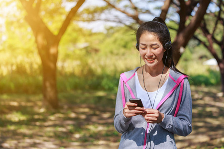 年轻的运动妇女使用智能手机与耳机在公园