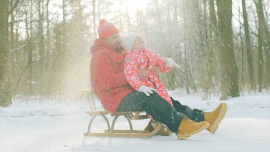 快乐的小男孩和他的祖父在雪下冬季公园的雪橇上