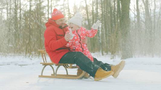 快乐的小男孩和他的祖父在冬天公园的雪橇上