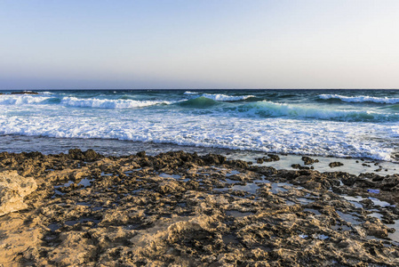 在塞浦路斯岛上夕阳的最后一缕波浪上, 暴风雨般的海浪在岩石的岸边折断。