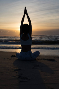 运动的年轻女子在海滩上做瑜伽的剪影, 健康生活的概念和身体与精神发展之间的自然平衡