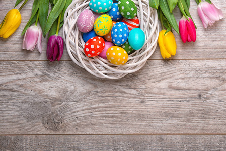 复活节彩蛋在一个柳条篮子与五颜六色的郁金香在木质背景。复活节假期概念