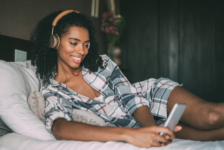 妇女在床上听音乐与耳机和智能手机