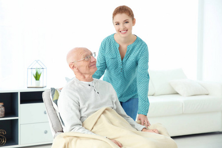 老人在扶手椅和年轻照顾者在家中