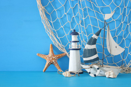 航海概念以白色装饰风帆小船灯塔海星海贝壳和鱼网在蓝色木桌和背景