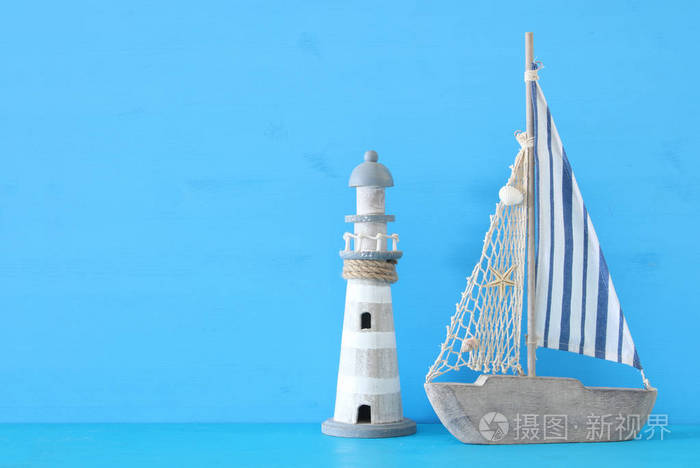 航海概念与白色装饰风帆小船和灯塔在蓝色木桌和背景