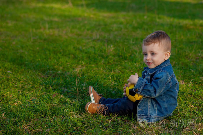 两岁男孩保持足球坐在草地上