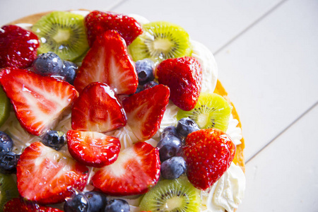 白色木桌上的奶油草莓蓝莓和猕猴桃的蛋糕上图