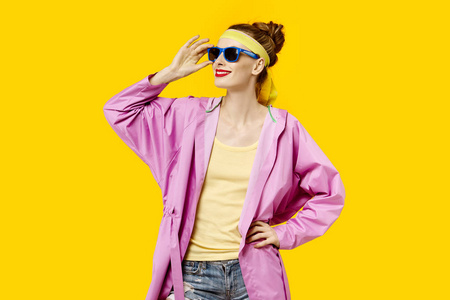 在黄色背景和粉红色外套和太阳镜的年轻妇女。色彩痴迷的概念。简约风格。时尚时尚
